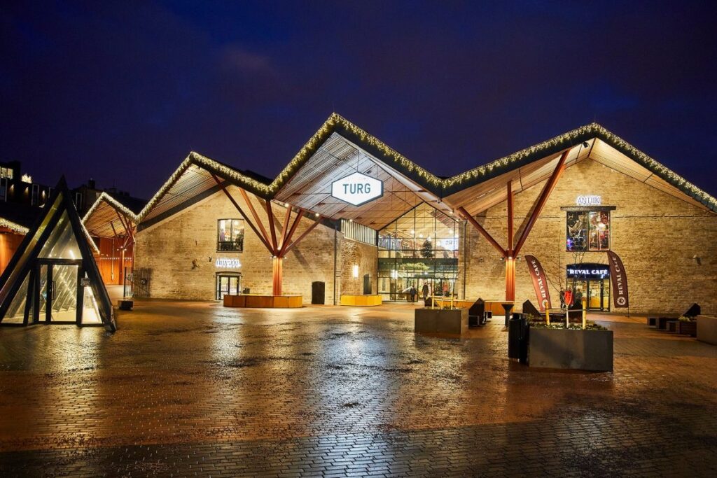 Balti Jaama Turu valgustatud hoone õhtupimeduses, modernsed katusekonstruktsioonid ja klaasfassaad.