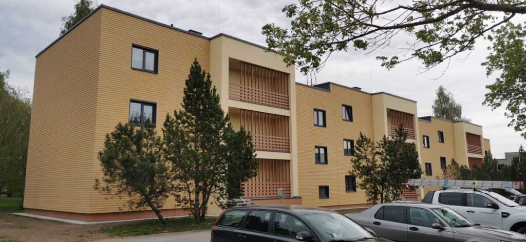 Renoveeritud kortermaja, millel on hele fassaad ja varjulised rõdud. Esiplaanil puud ja pargitud autod.